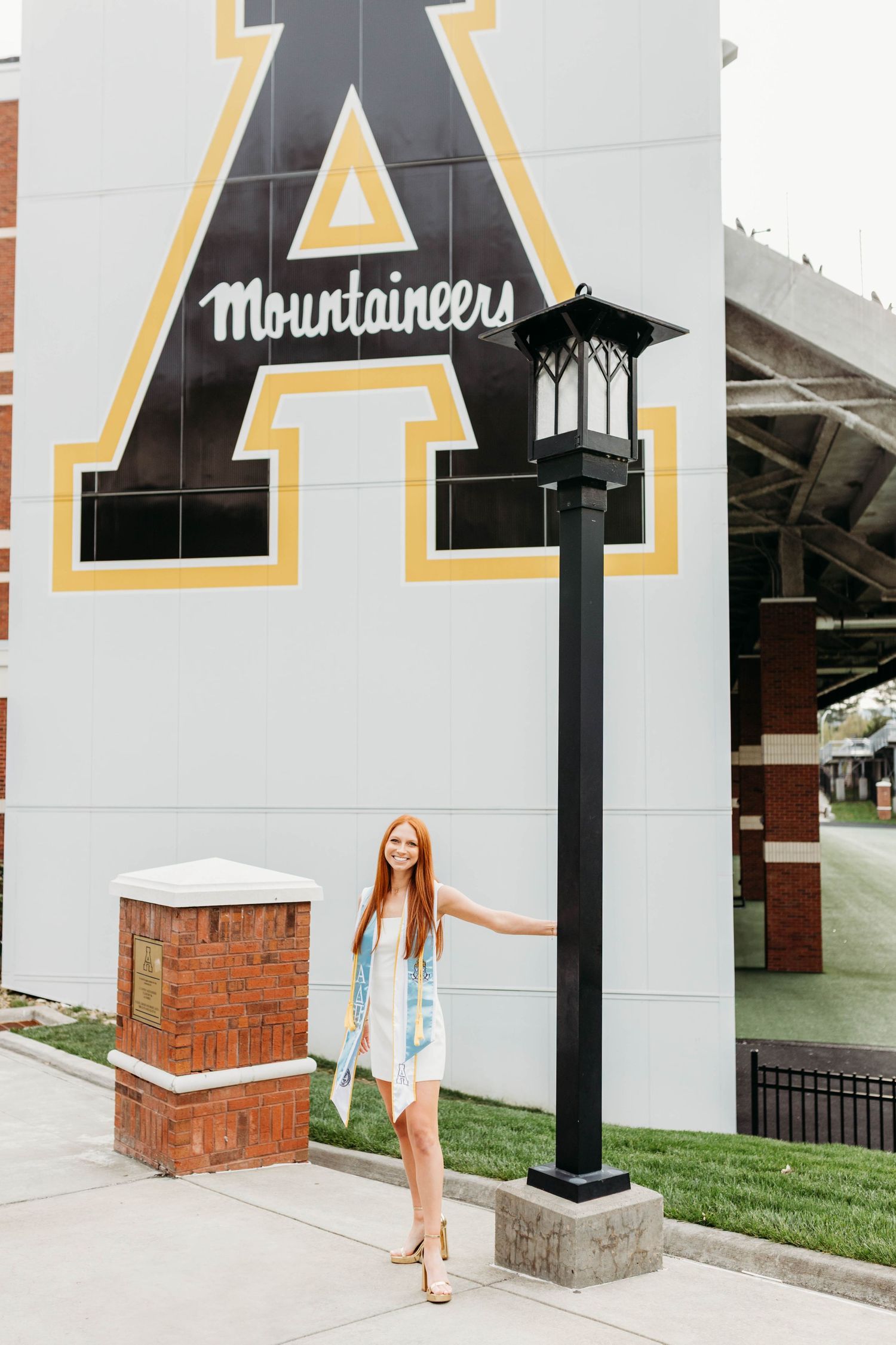 Graduate poses in front of large university logo wall with Mountaineers text.