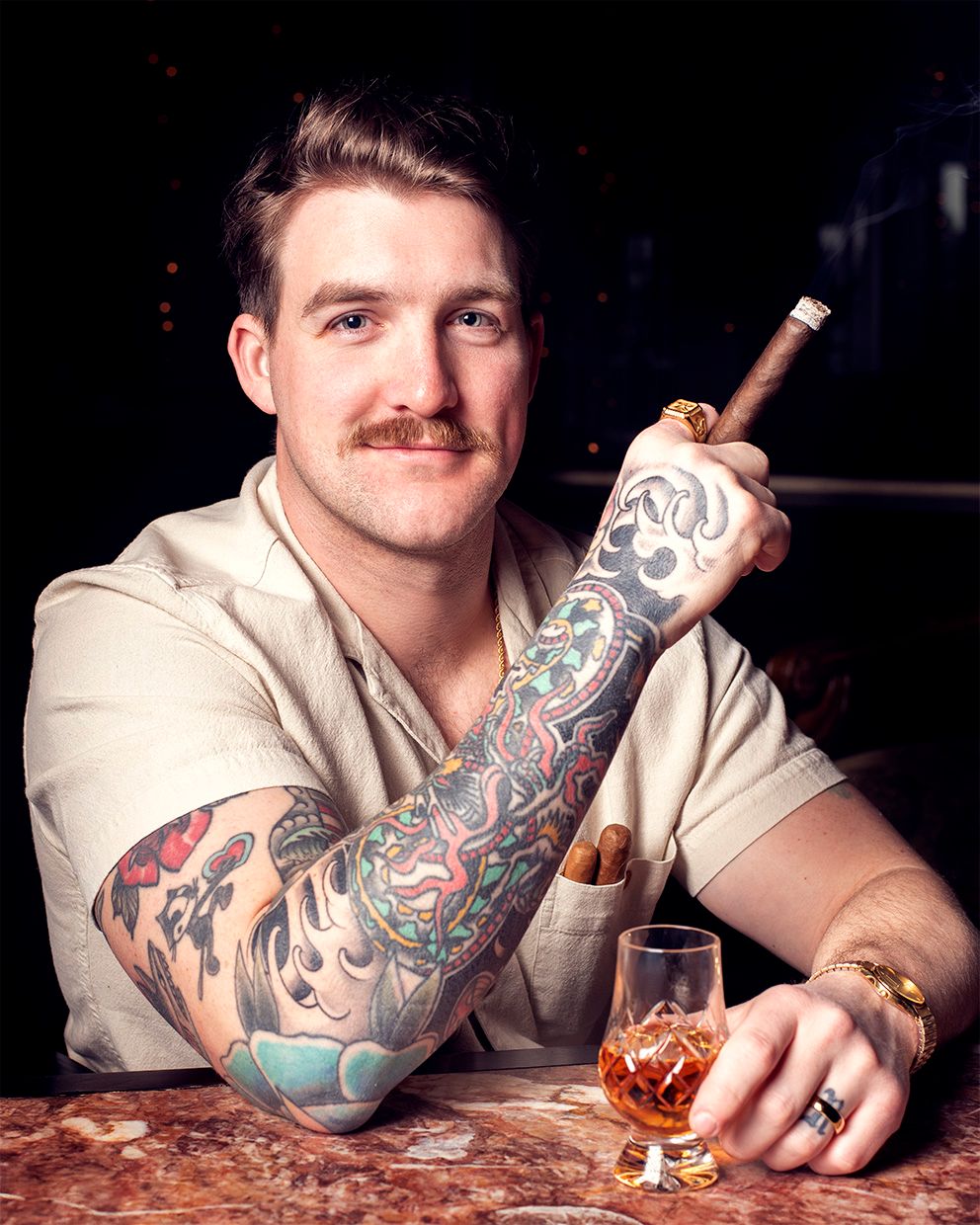 Man with mustache and tattoo sleeve enjoying drink at bar counter.