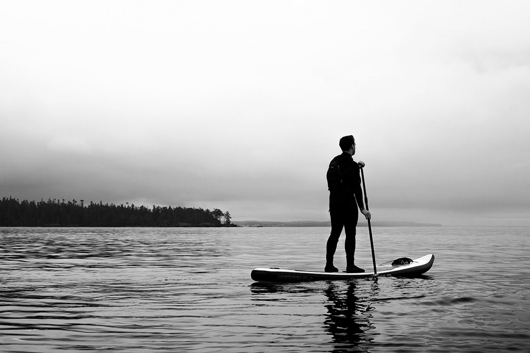 Silhouette of paddle boarder standing on board at sunset over calm waters.