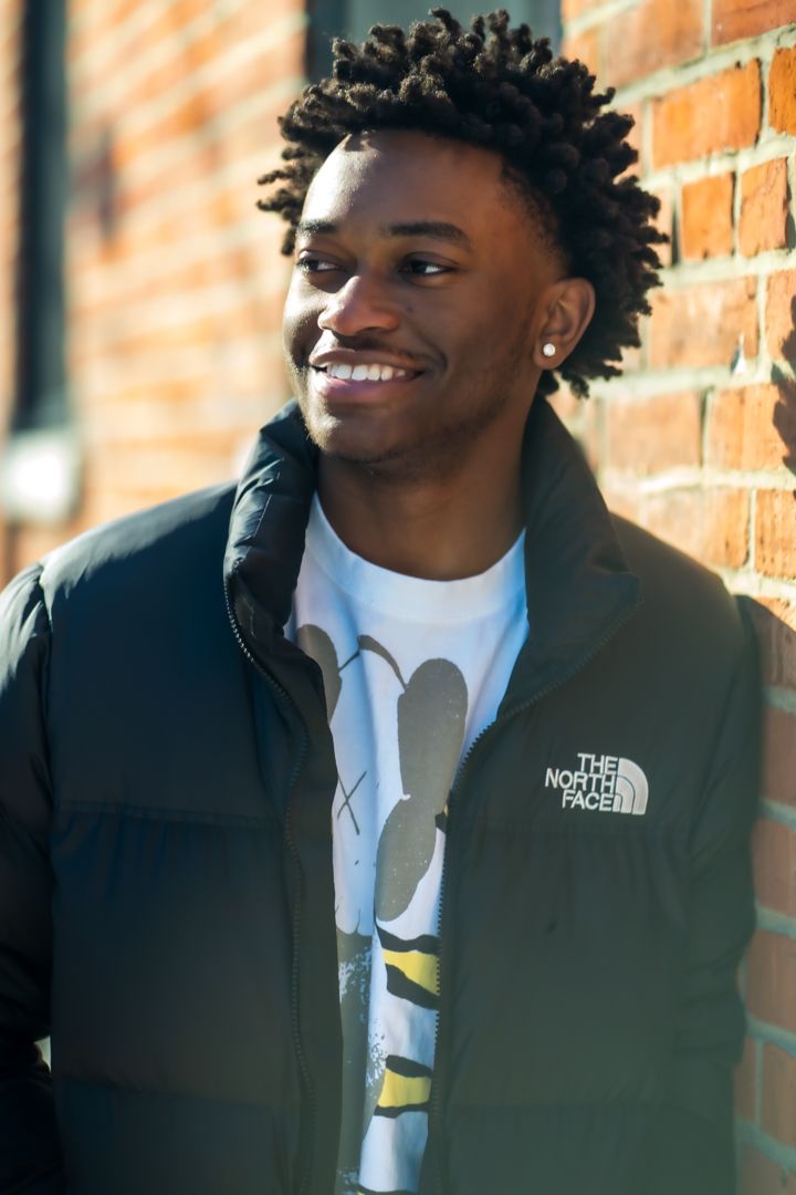 A smiling portrait against a brick wall wearing a North Face jacket, white shirt and an earring.