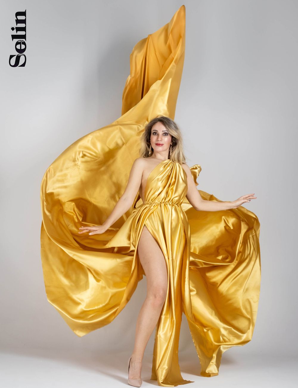 Dramatic fashion photo of gold silk dress flowing against gray studio background.