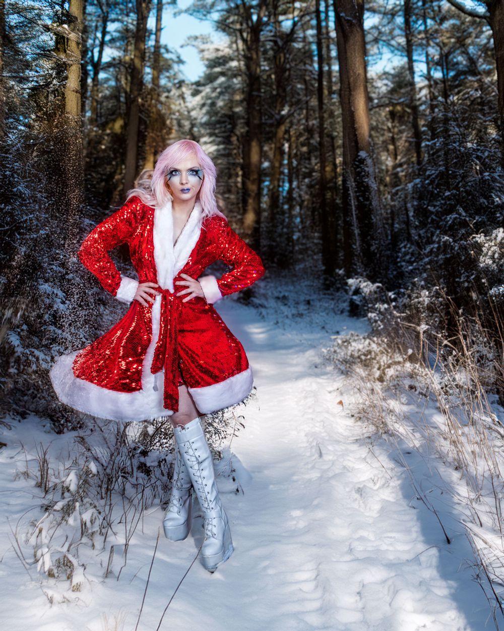 Festive red and white holiday dress worn in a snowy forest setting with tall evergreen trees.