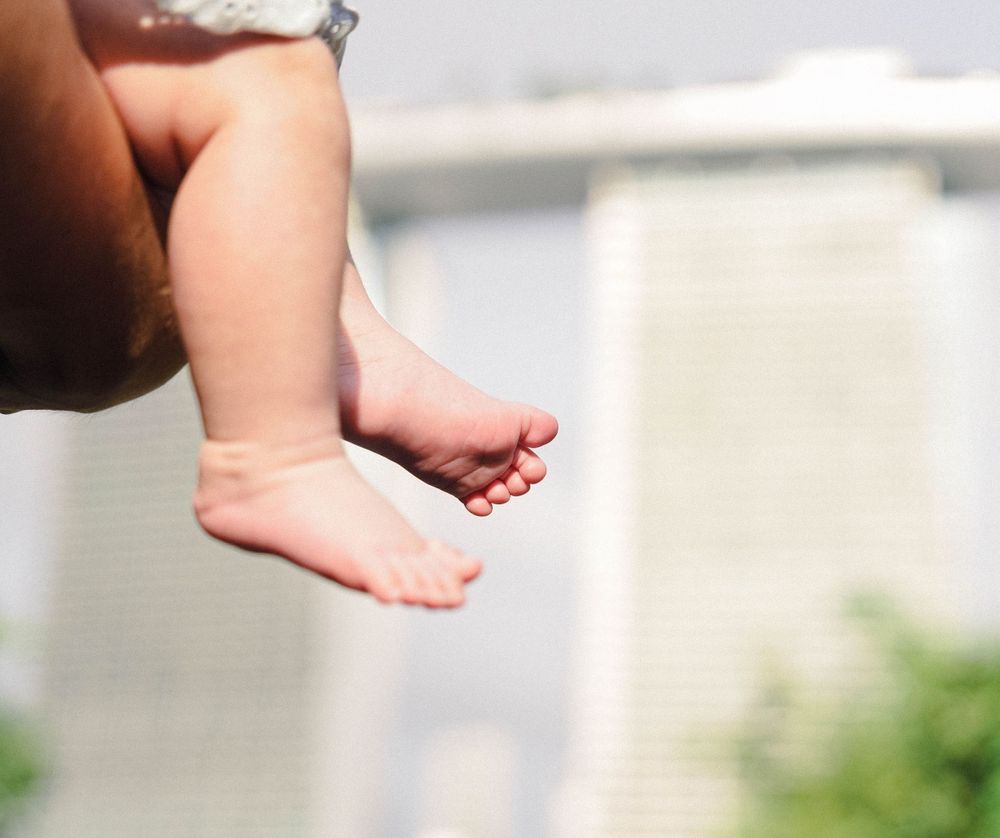 A close-up view of tiny bare baby feet dangling in soft sunlight against a blurred background.