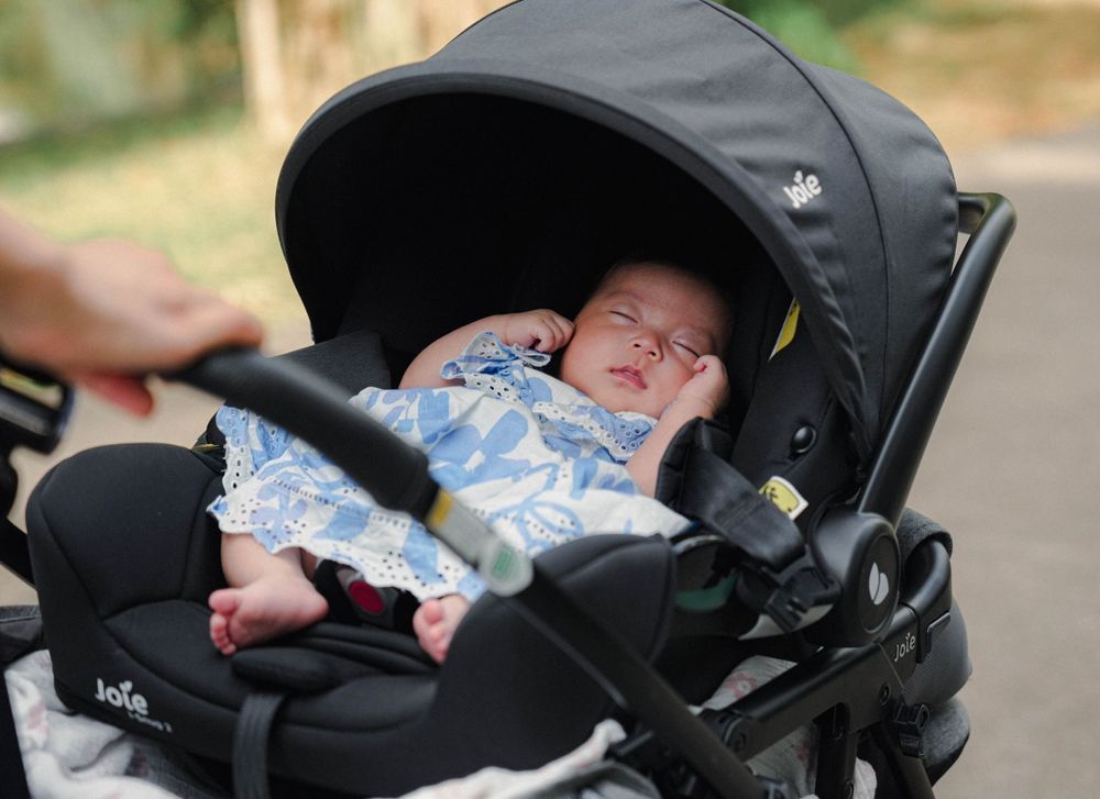 A baby sleeping peacefully in a black stroller wearing a blue patterned outfit.