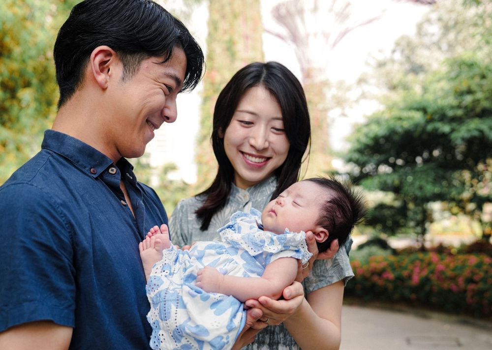 A happy couple shares a tender moment while holding their newborn baby outdoors in a garden setting.