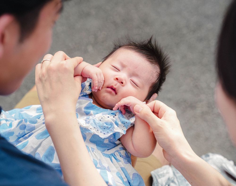 A tiny baby in a blue floral outfit receives oral medication from a caregiver.