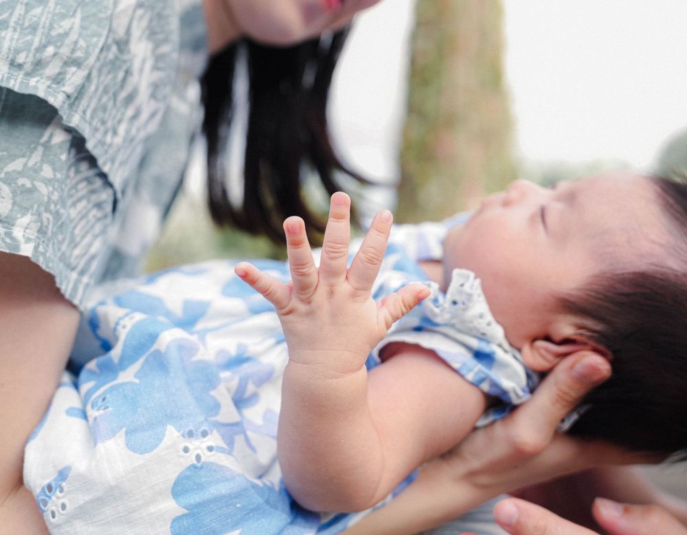 A baby in a light blue floral outfit reaches their tiny hand up while lying with their caregiver.
