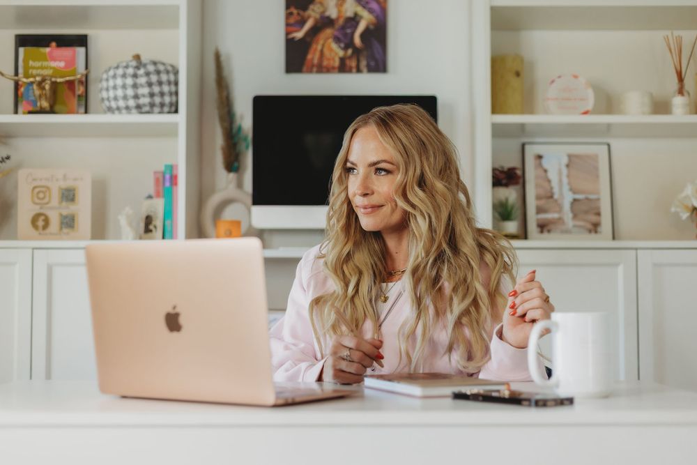 A feminine workspace with a rose gold laptop, white desk, and decorative accessories arranged in a clean, modern style.