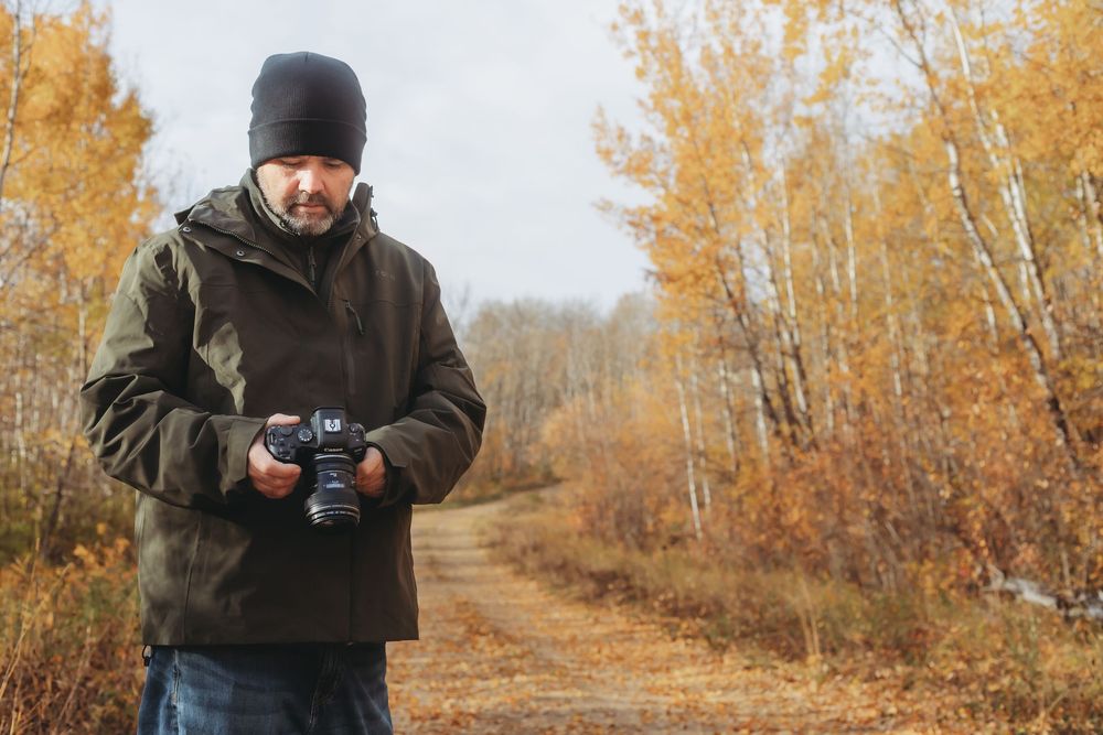 Photographer capturing autumn scenery along a tree-lined path with golden yellow foliage.