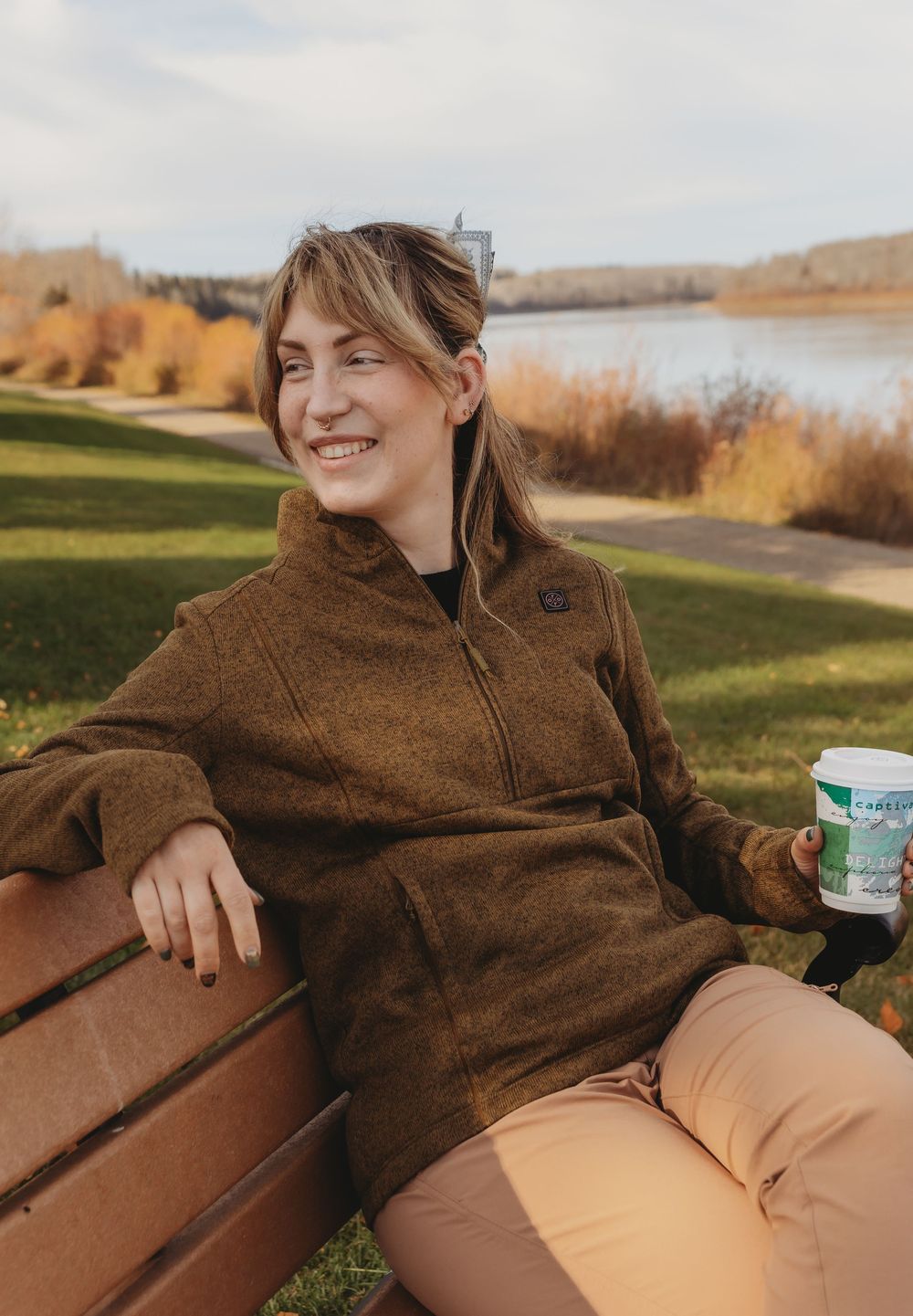 Person relaxing on a park bench wearing a brown sweater and khaki pants on an autumn day by the water.