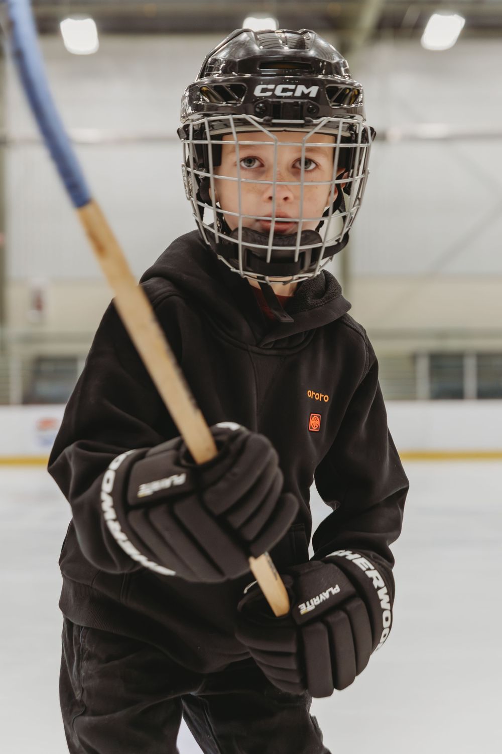 Hockey player in black uniform and helmet skates on ice while holding a hockey stick during practice.