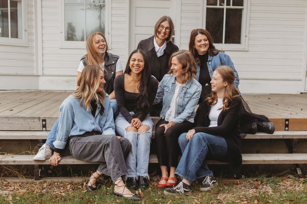 A group of people sitting together on wooden porch steps wearing casual denim and autumn clothing.