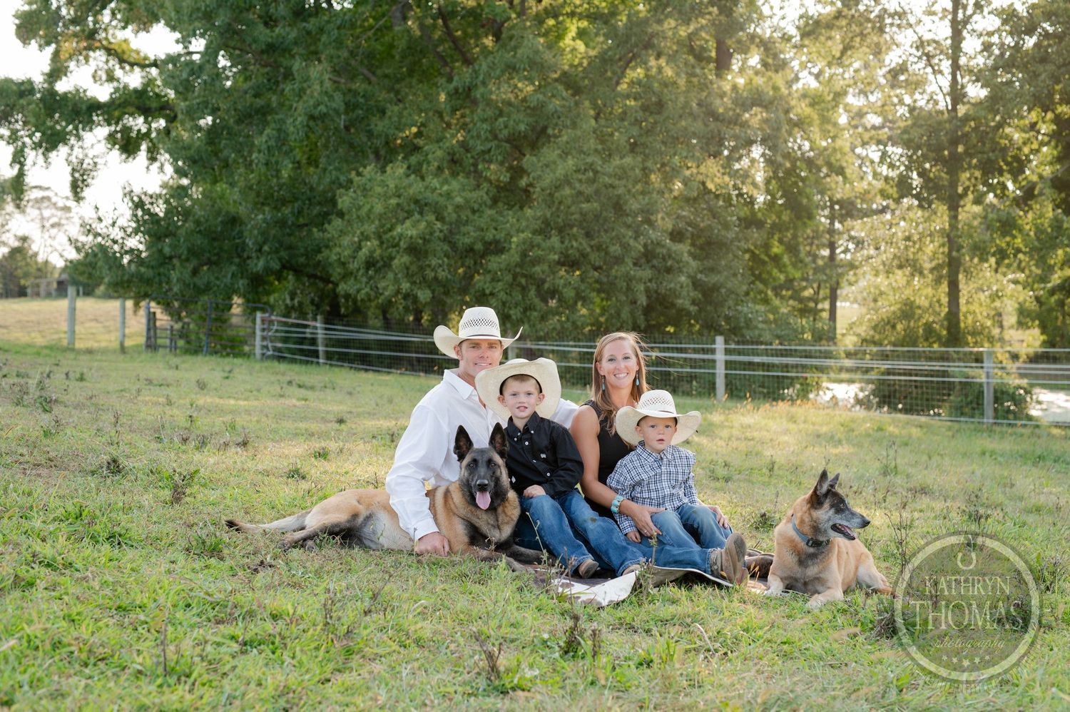Family sitting together on grassy hillside with their German Shepherd dogs during golden hour.