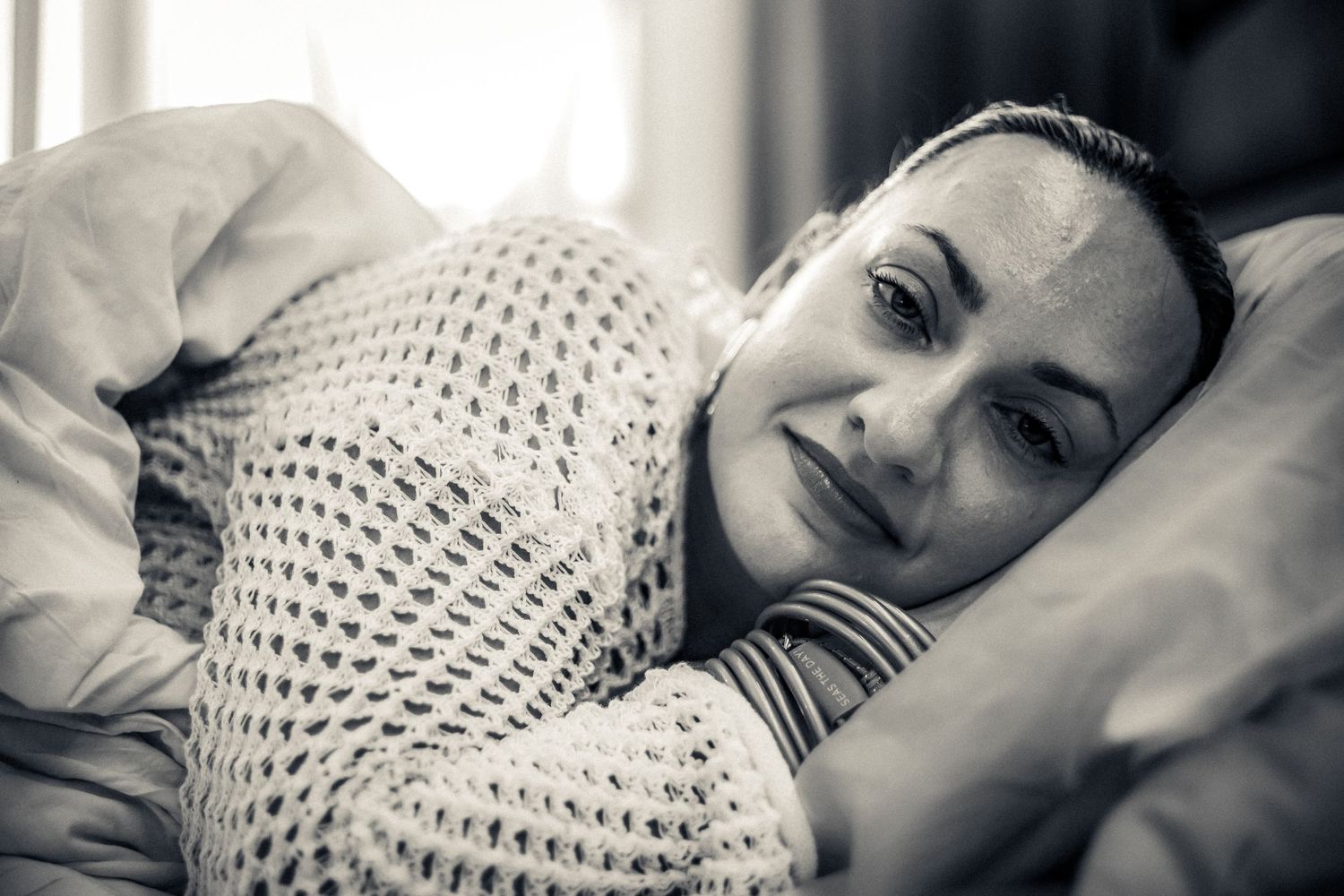 Black and white portrait of someone resting on pillows while wrapped in a cozy knit blanket.