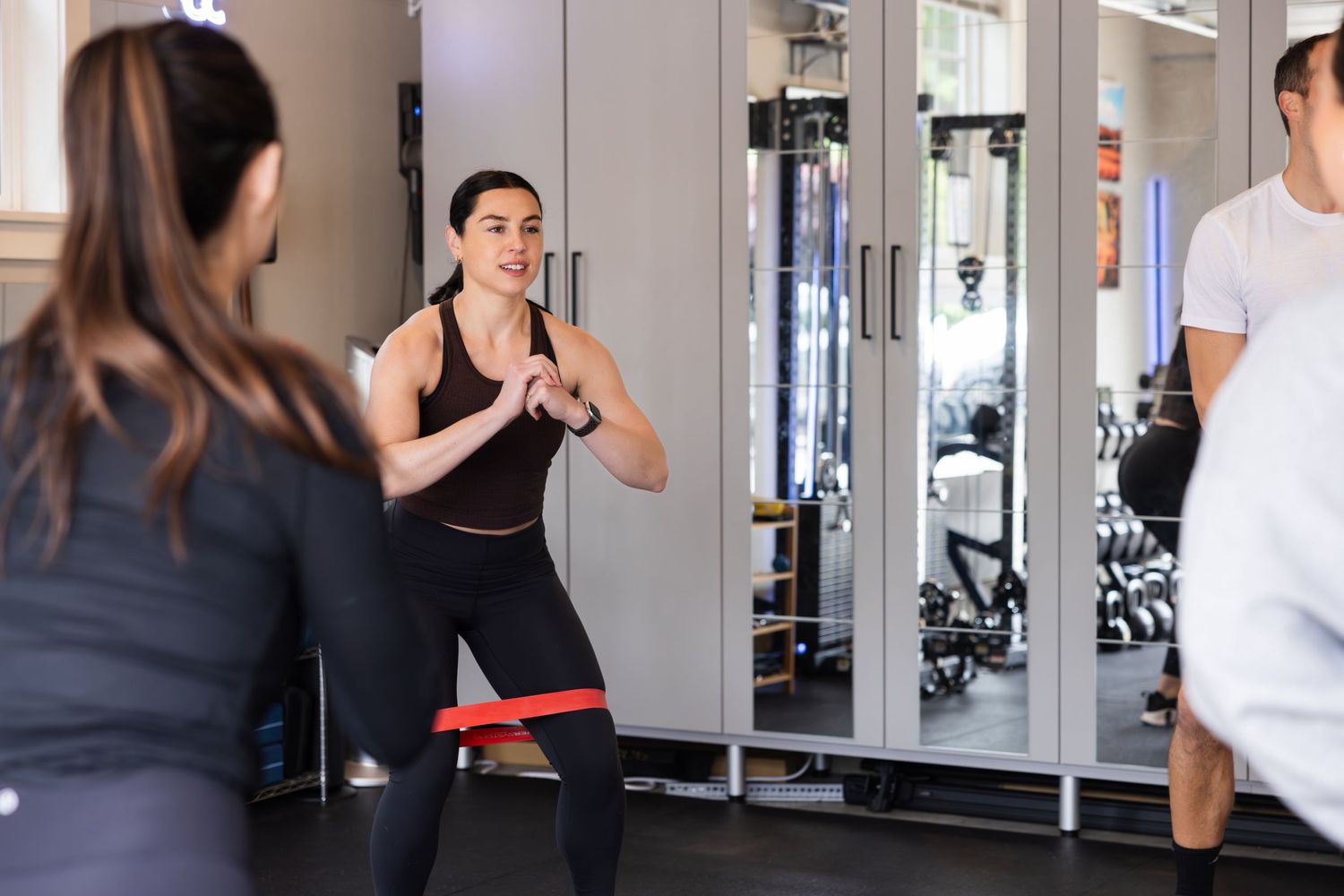 Group exercise session with participants working out together in a modern fitness gym with mirror walls.