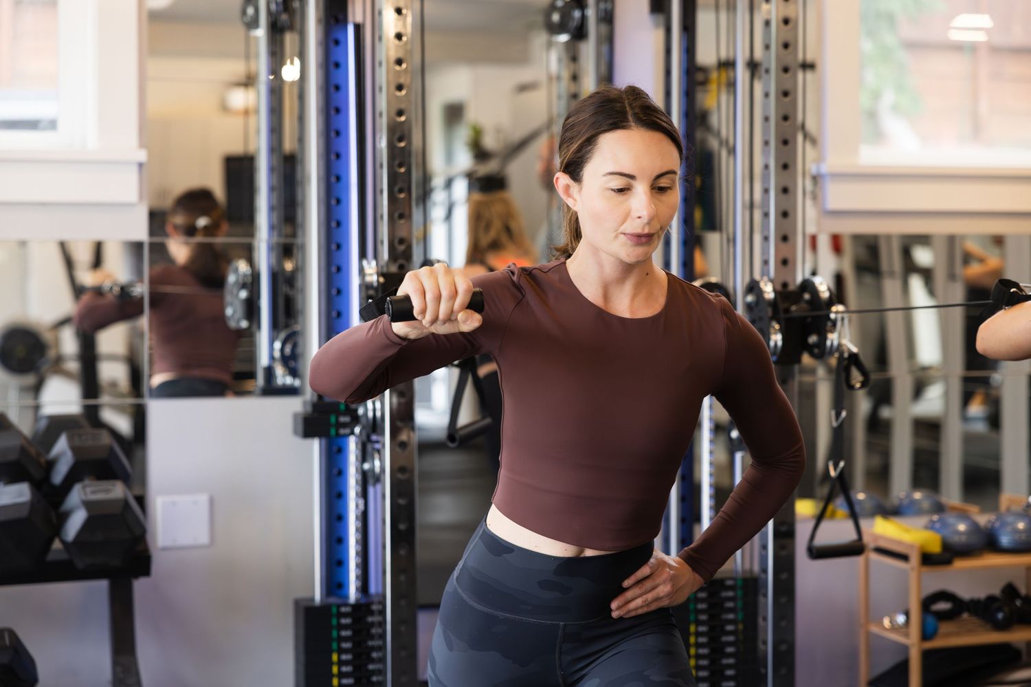Active person working out on exercise equipment at a modern fitness center wearing brown long sleeve top and dark pants.