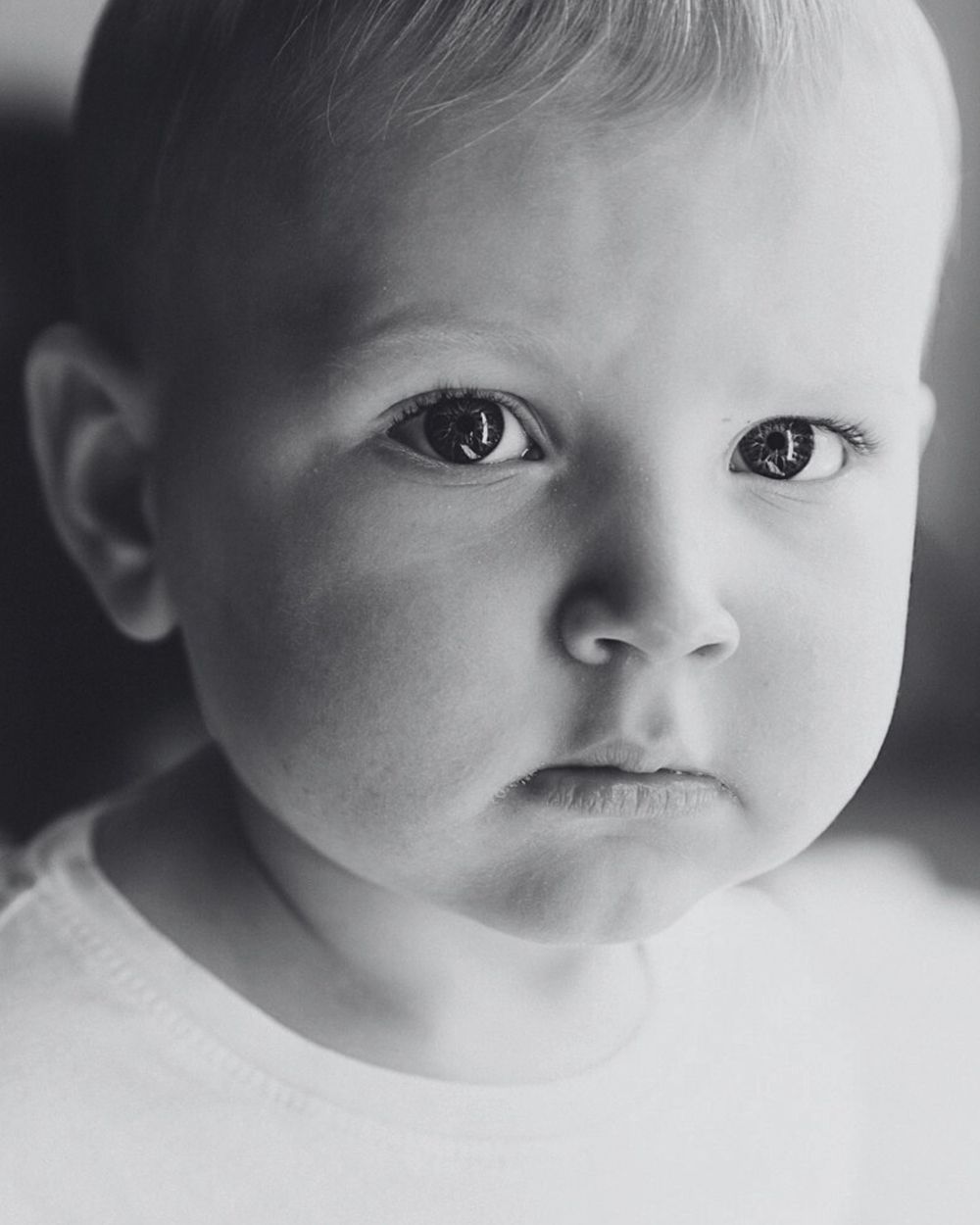 Black and white studio portrait of a sweet faced baby in a white garment looking at the camera.