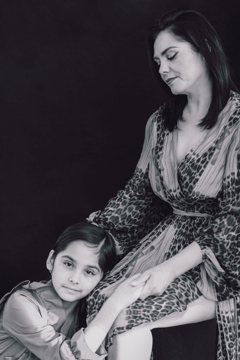 Black and white portrait showing an intimate moment between a parent and child, with the child hugging the parent's side.