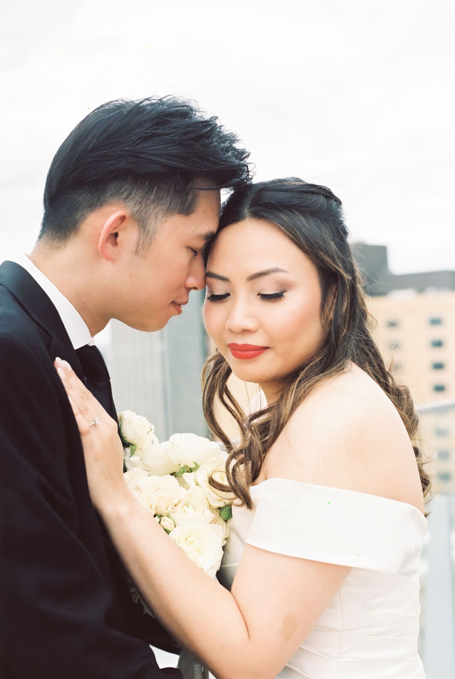 A romantic wedding couple shares an intimate moment with the bride in an off-shoulder dress holding white flowers.