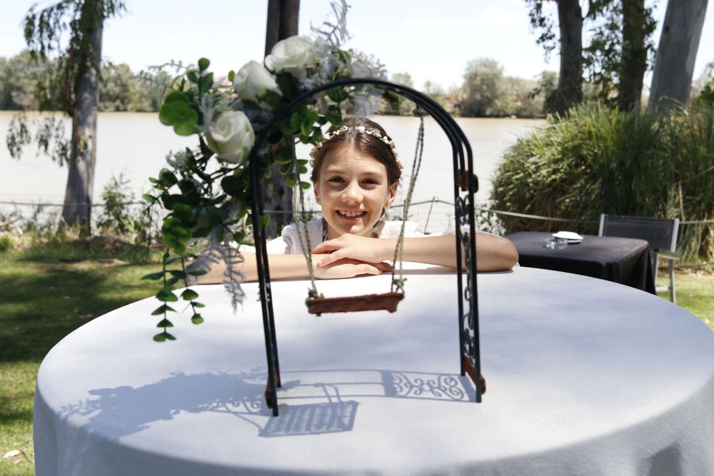 A decorative black metal arch with white flowers and greenery sits atop a round white table outdoors.