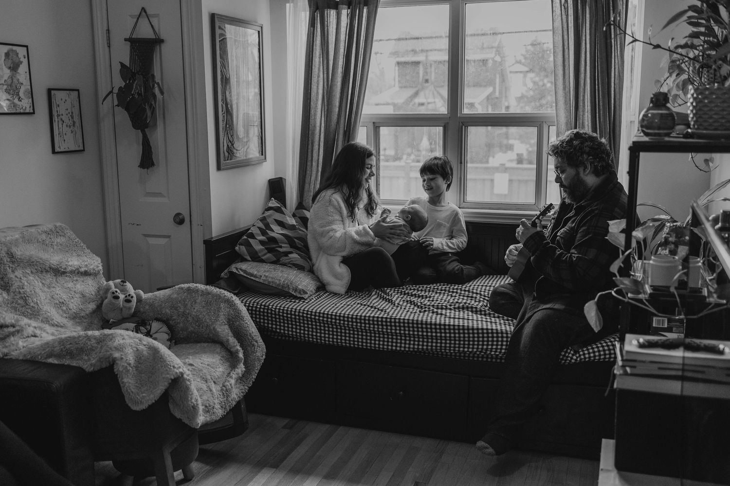 family of four hanging out close to the window in the living room while the father plays guitar, in Etobicoke, Toronto