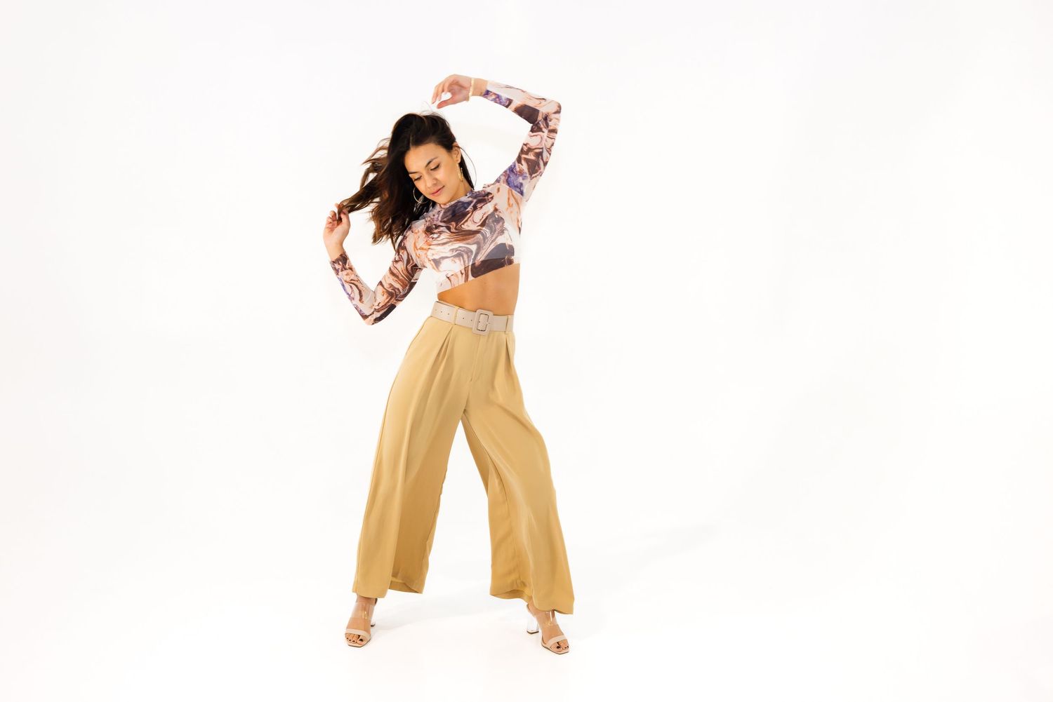 A dancer in yellow wide-leg pants and a floral crop top strikes a dynamic pose against a white background.