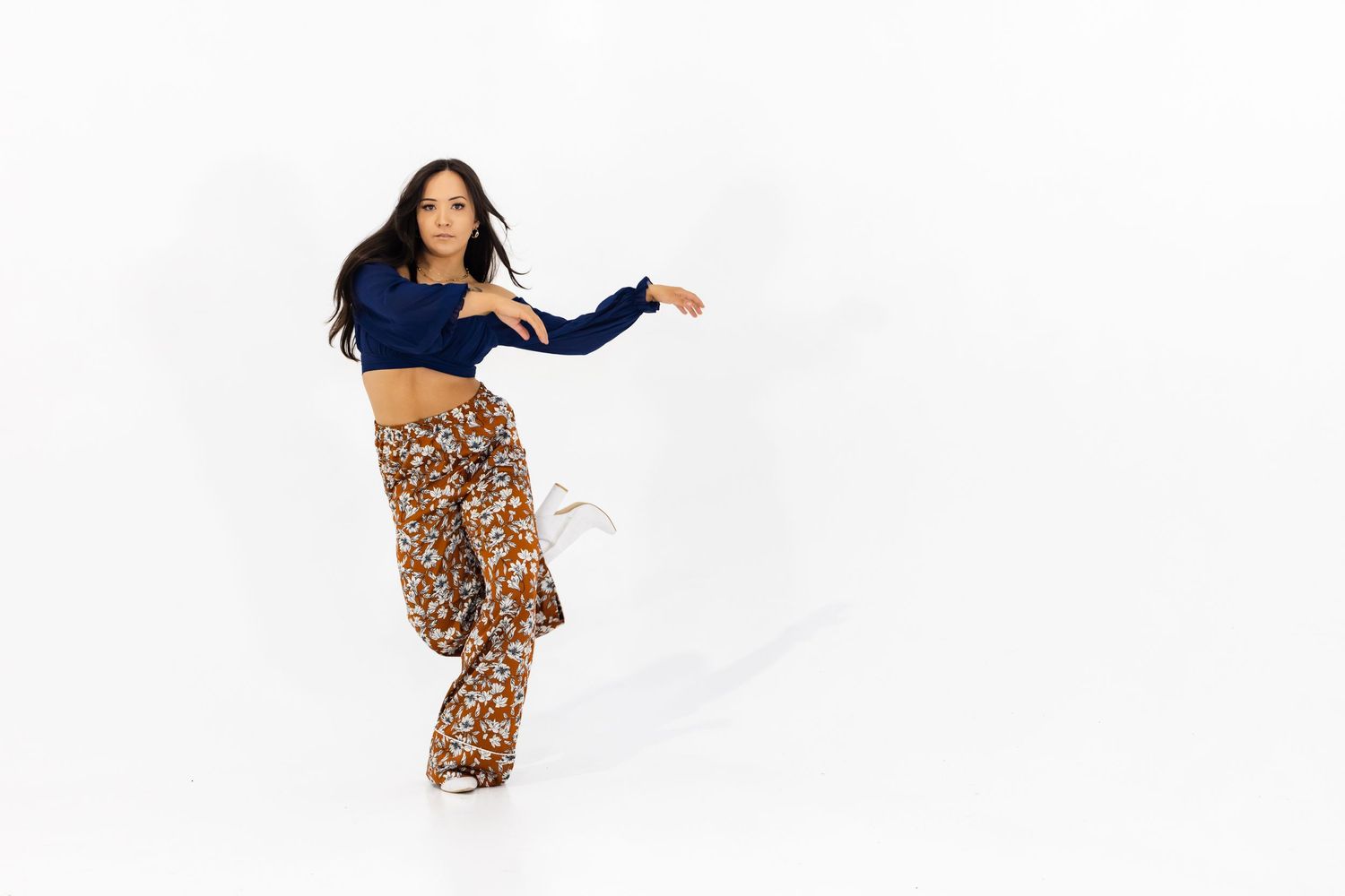 A dancer in a navy crop top and floral print pants moves gracefully against a white studio background.