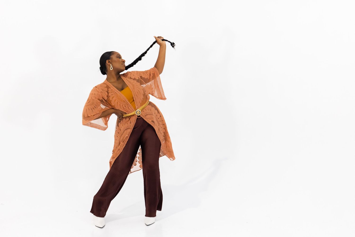 A performer in an orange coat dances gracefully with expressive arm movements against a white background.