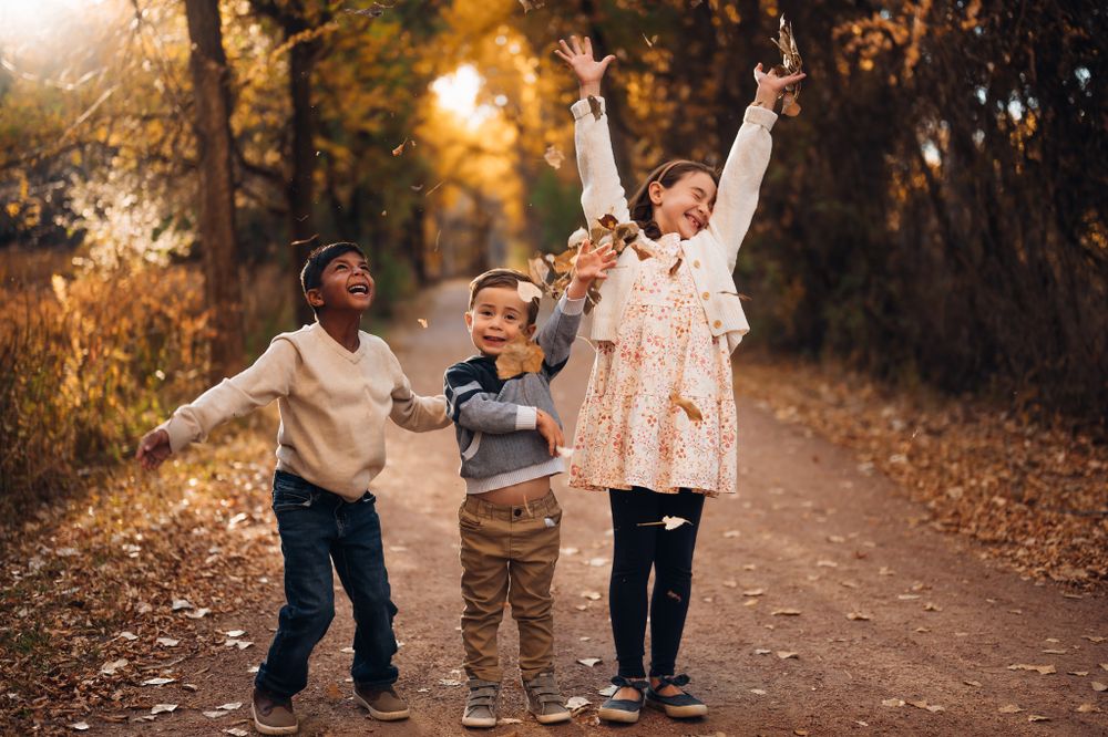 Three children running and jumping with arms raised on autumn path. Fall family photography in canon city Colorado