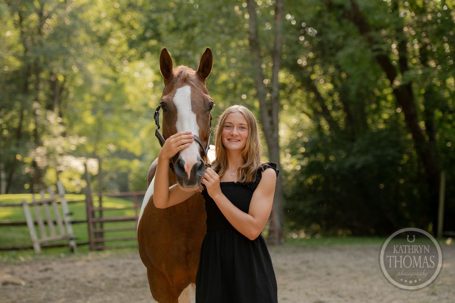 A person in a black dress poses with their paint horse during an outdoor photo session.