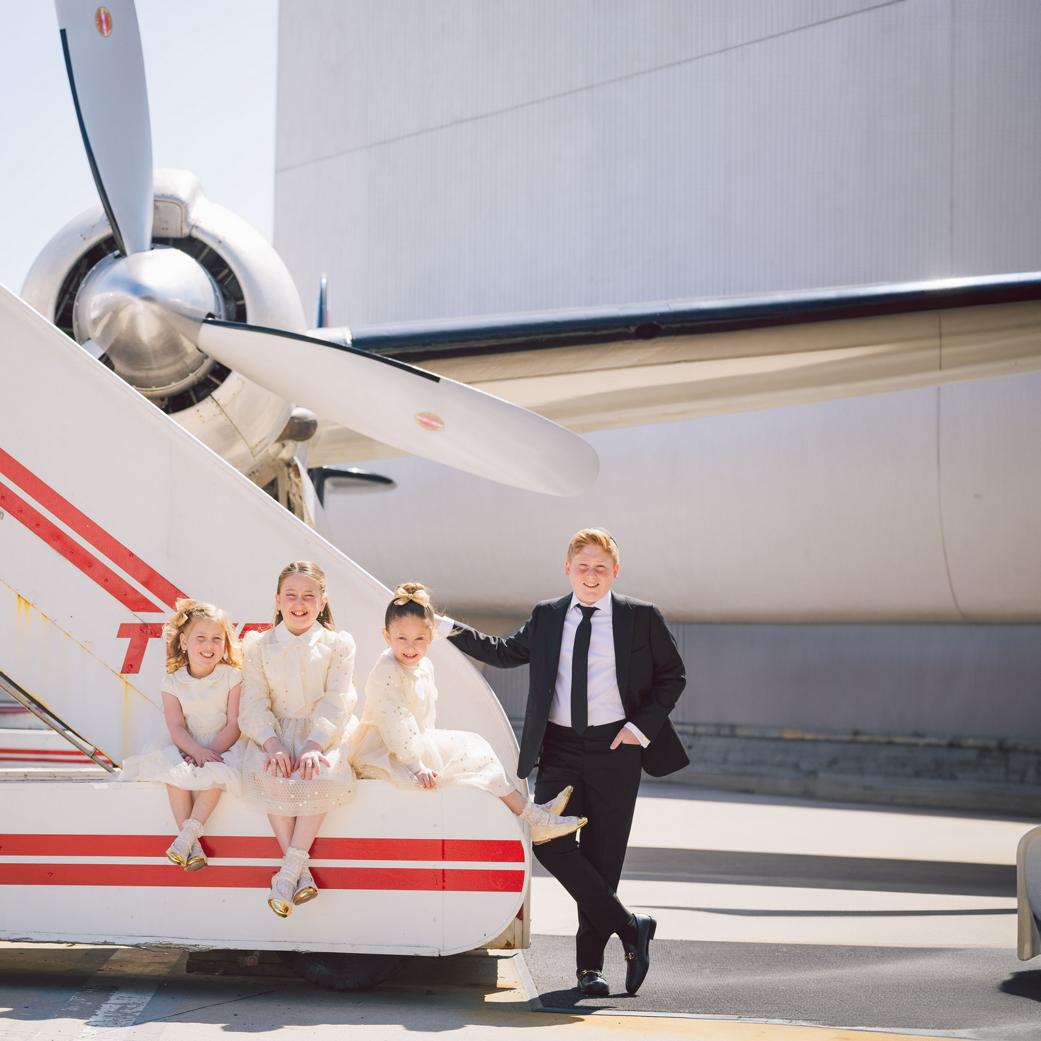 Wedding party posing playfully near a small private aircraft on a sunny day.