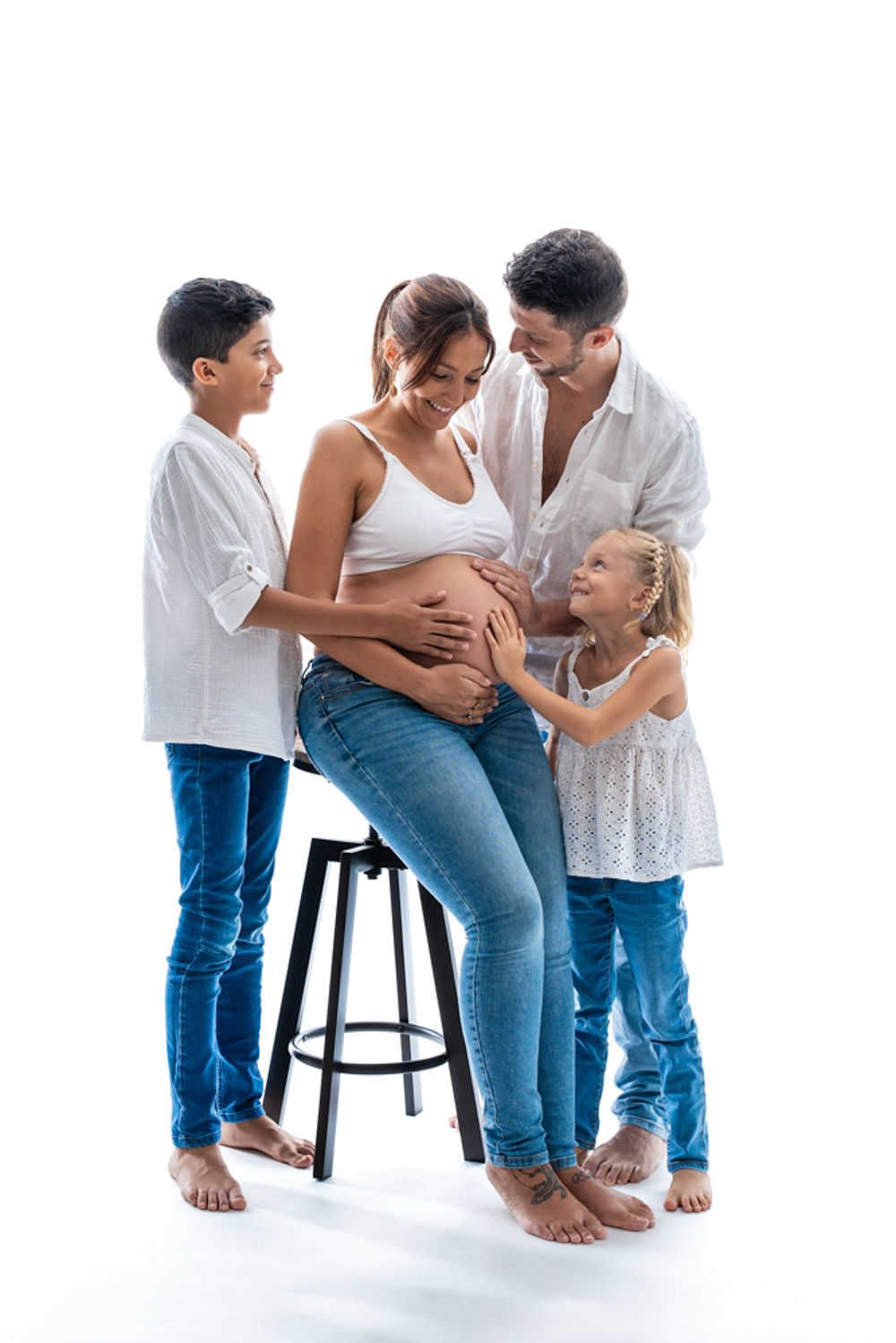Une famille en tenues blanches et bleues partage un moment intime ensemble lors d'une séance photo de maternité sur fond blanc.