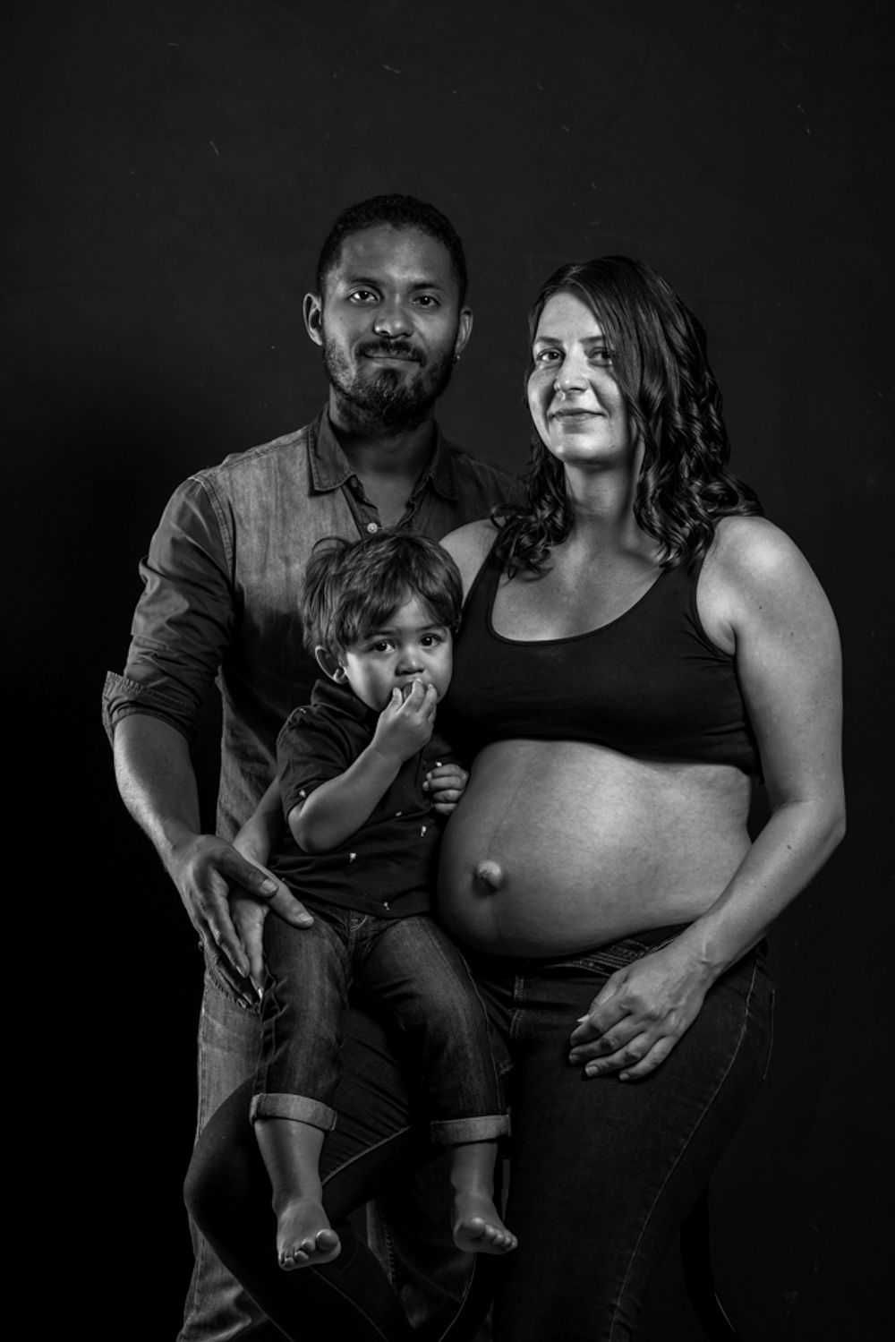 Portrait en noir et blanc d'une famille de trois personnes en attente d'un enfant sur fond sombre.