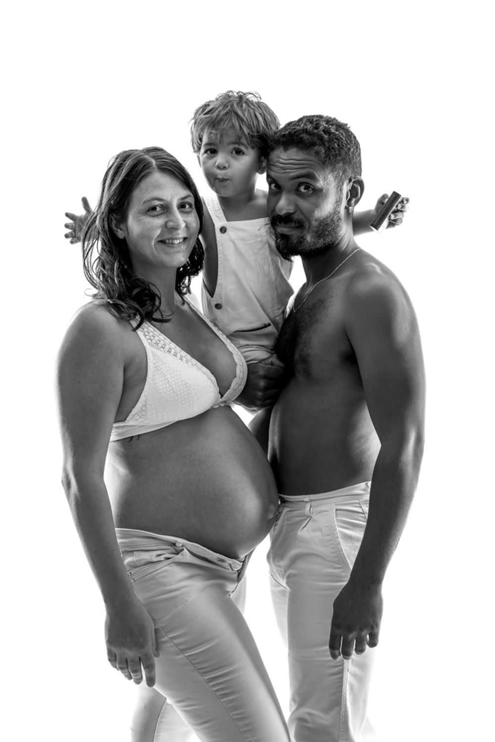 Portrait en noir et blanc d'une famille enceinte portant des vêtements blancs sur un fond simple.