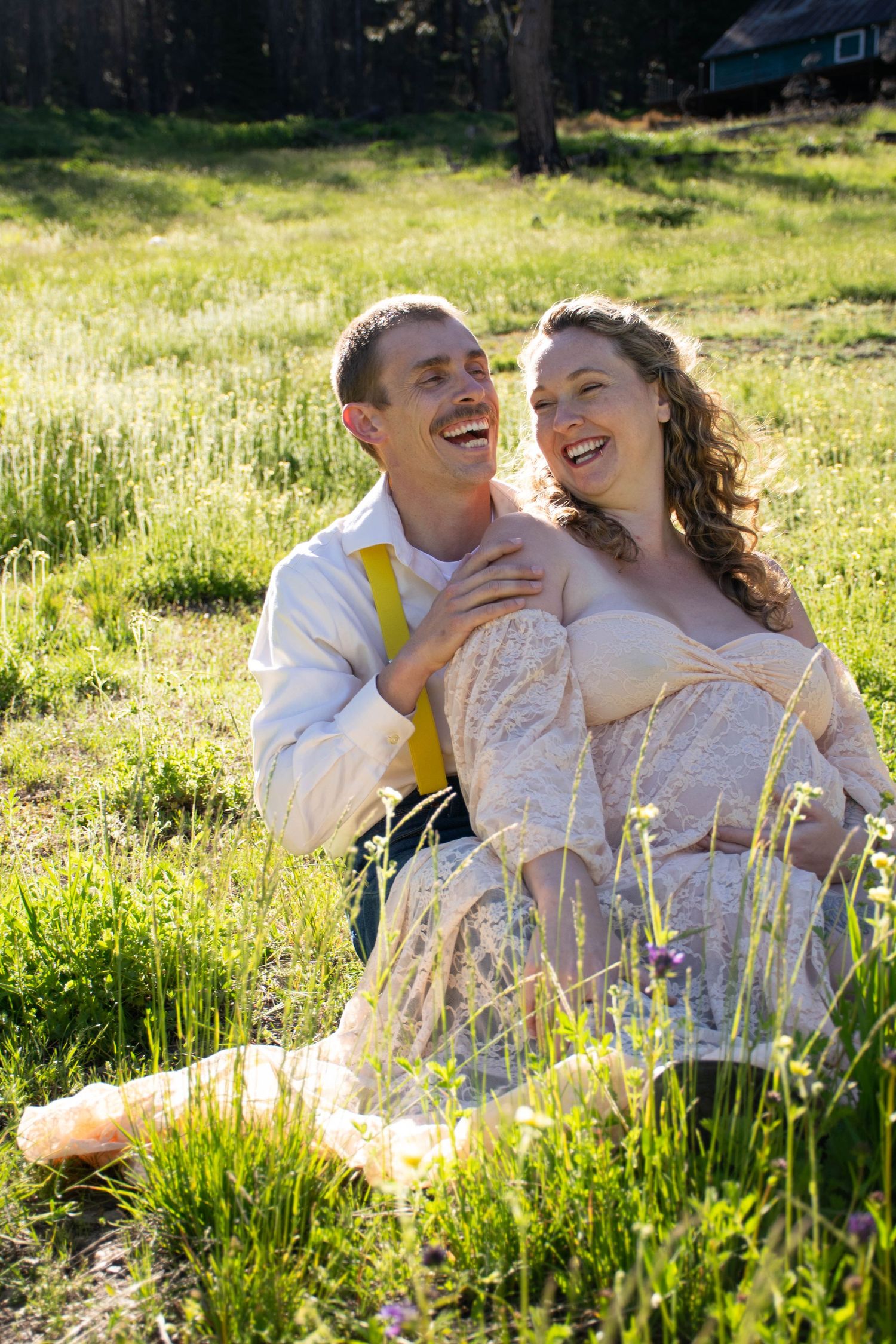 Couple laughing together in sunny meadow wearing formal attire.