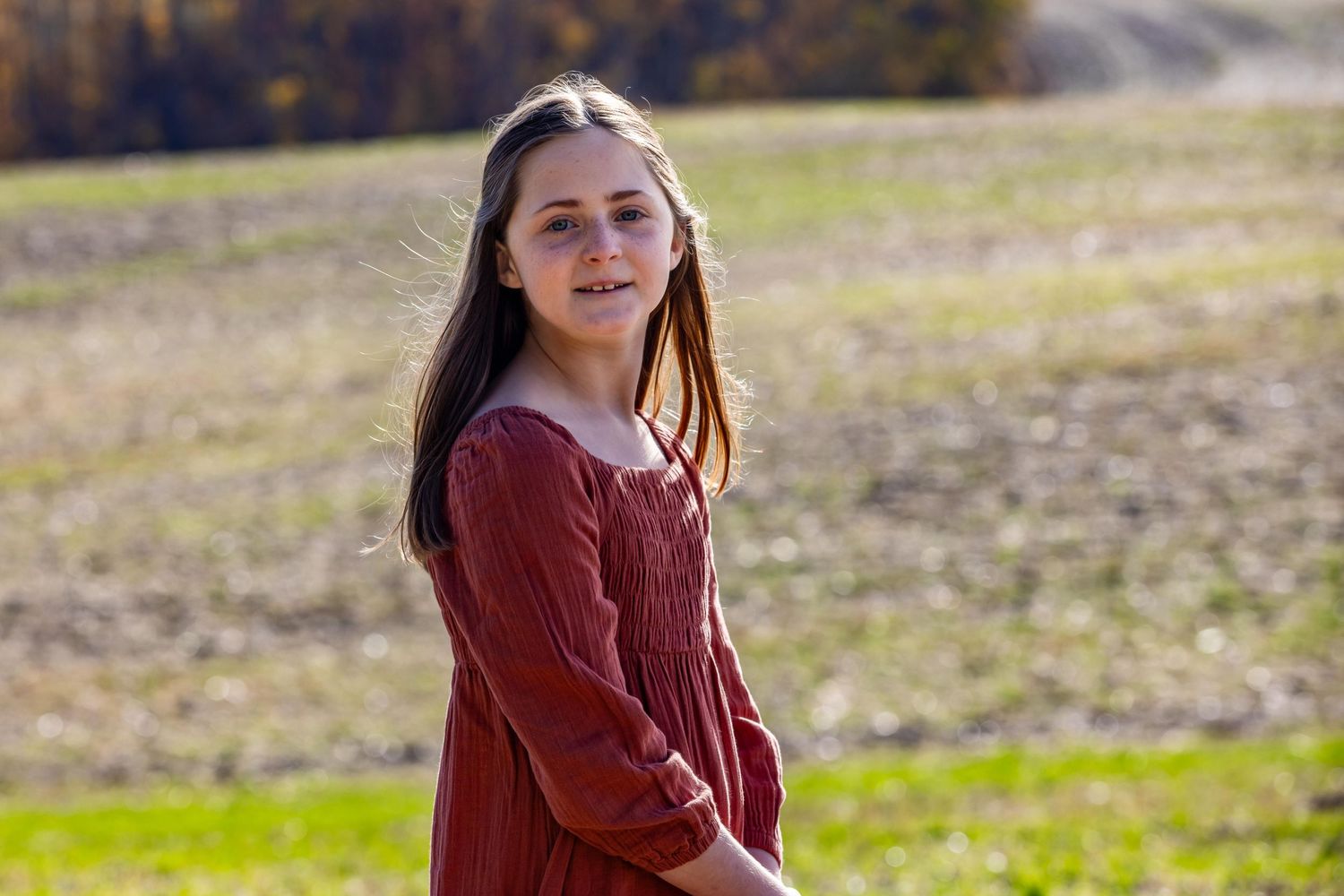 A person wearing a burgundy sweater standing in an autumn field on a sunny day.