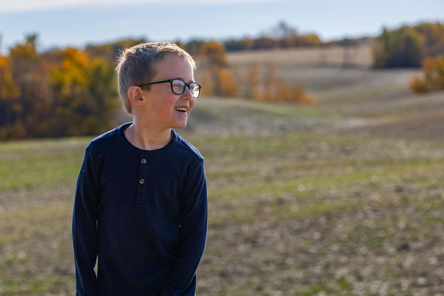 Person in glasses and navy sweater looks off into distance on a sunny autumn day in open field.
