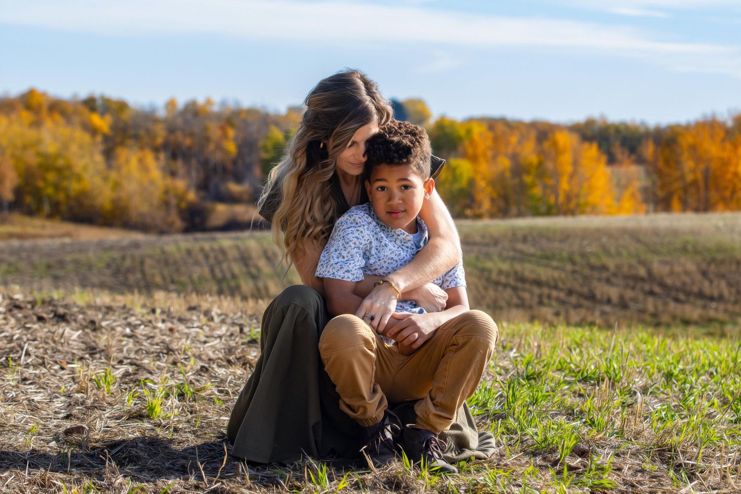Two people share a tender moment while sitting together in a sunny autumn field.