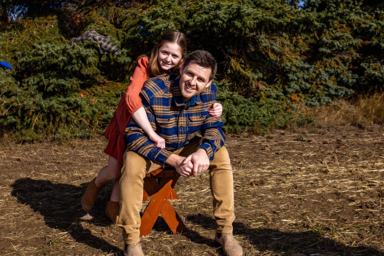 Two people share a tender moment sitting together on a log with autumn trees in the background.