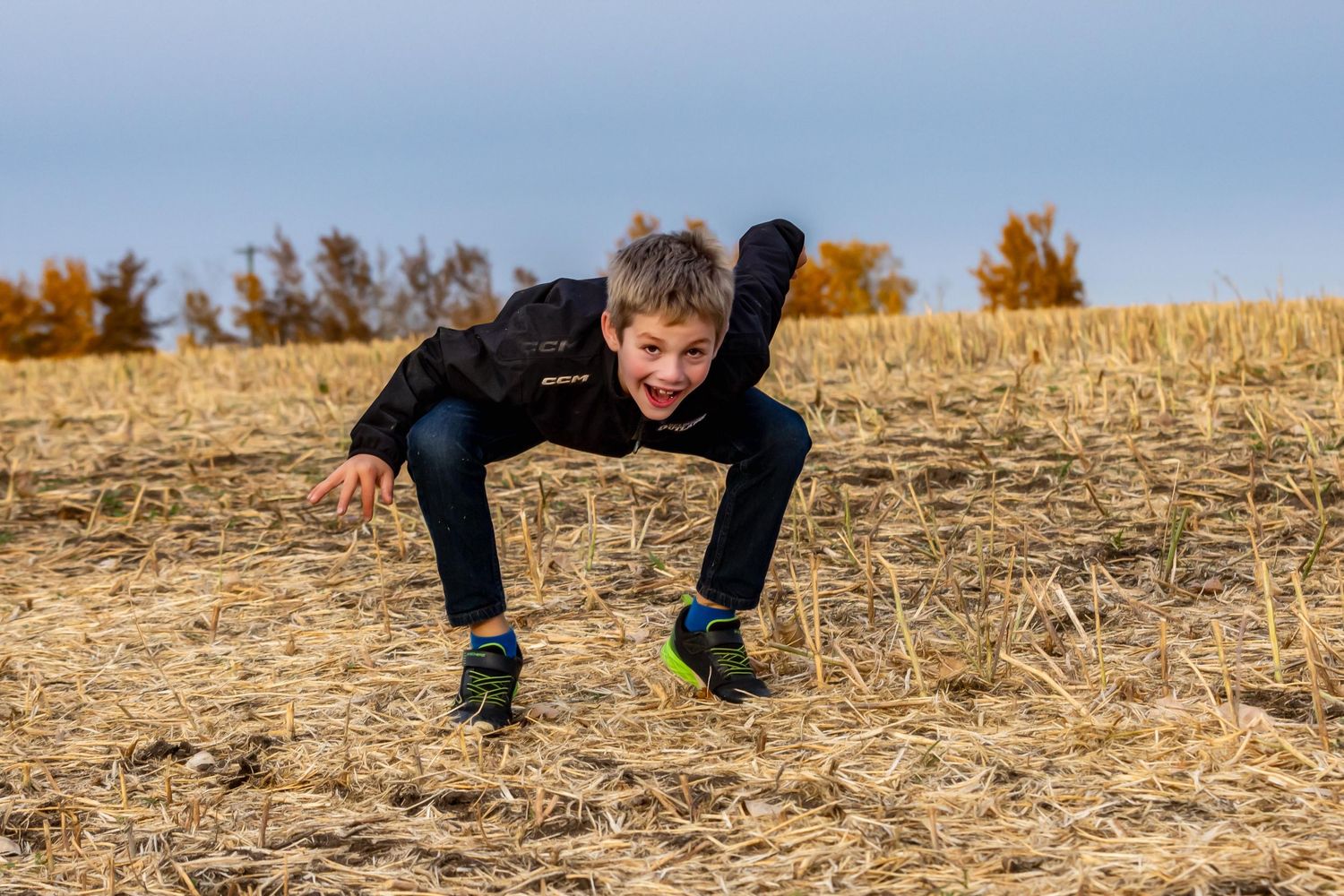 Someone in black athletic wear performs a dynamic parkour move on a dried field during autumn.