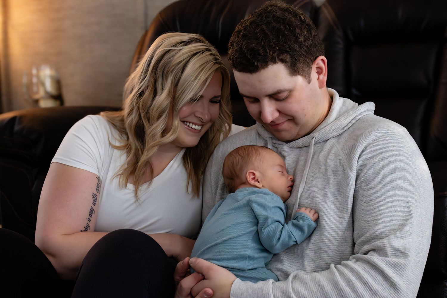 New parents share an intimate moment with their sleeping newborn baby while sitting together on a couch.