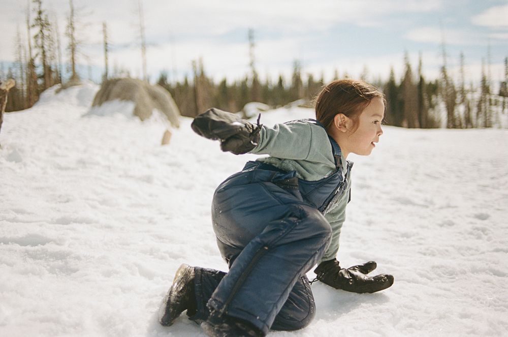 Someone in denim overalls crouching in the snow during a winter adventure.