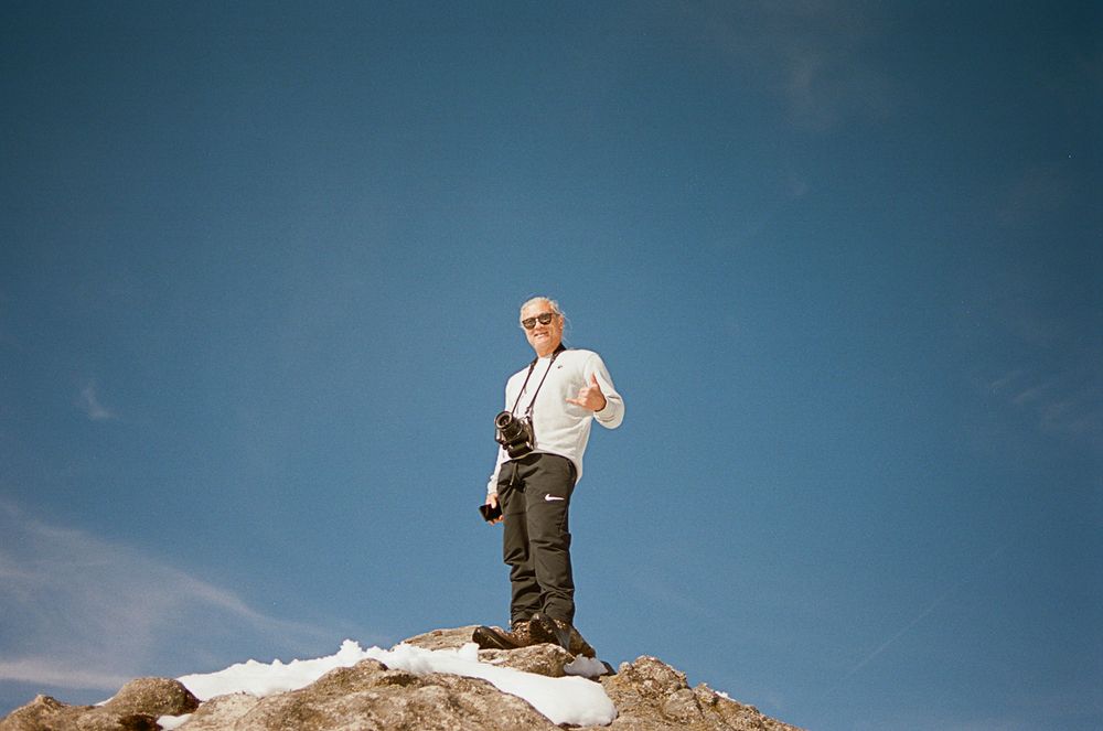 A person stands on top of a rocky outcrop against a bright blue sky.