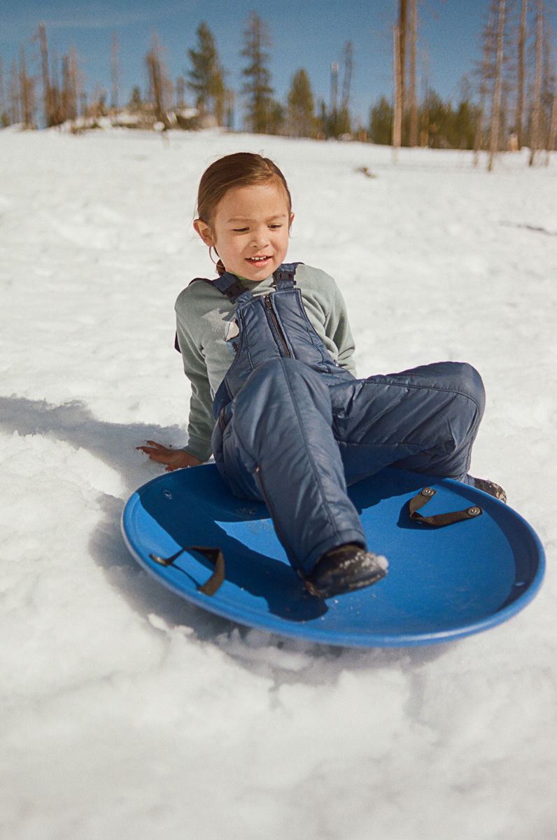 A joyful winter scene of sledding down a snowy hill on a bright blue disc sled.