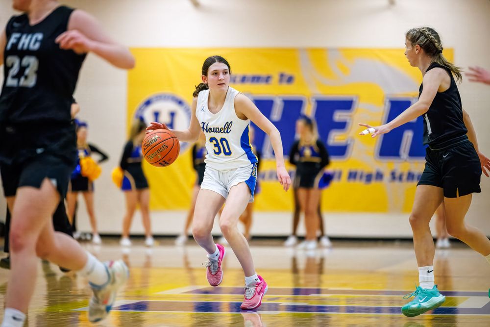 Basketball player wearing number 30 in white jersey dribbles past defenders during indoor game on yellow court.