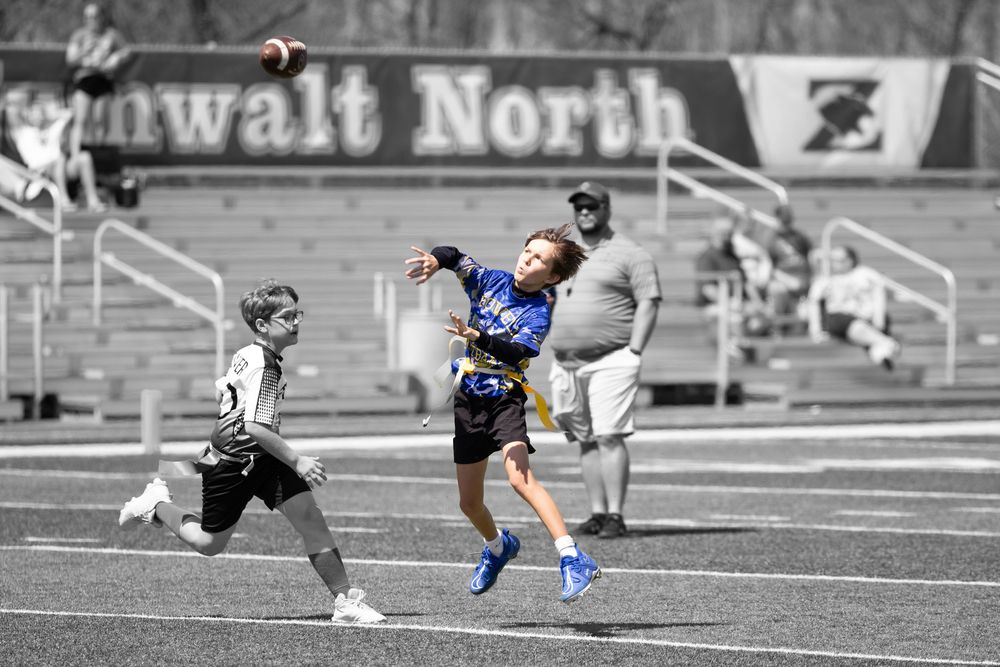 Ultimate frisbee player in blue jersey leaps high to catch disc during competitive match on turf field.