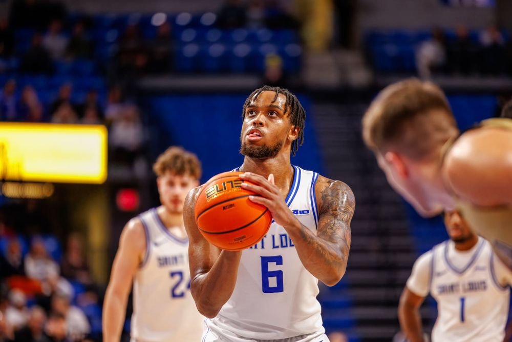 Basketball player in light colored jersey number 6 prepares to shoot during a game in an indoor arena.