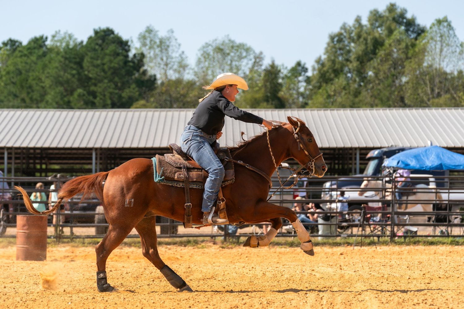 Horse and rider perform barrel racing maneuver in sandy arena during competition.