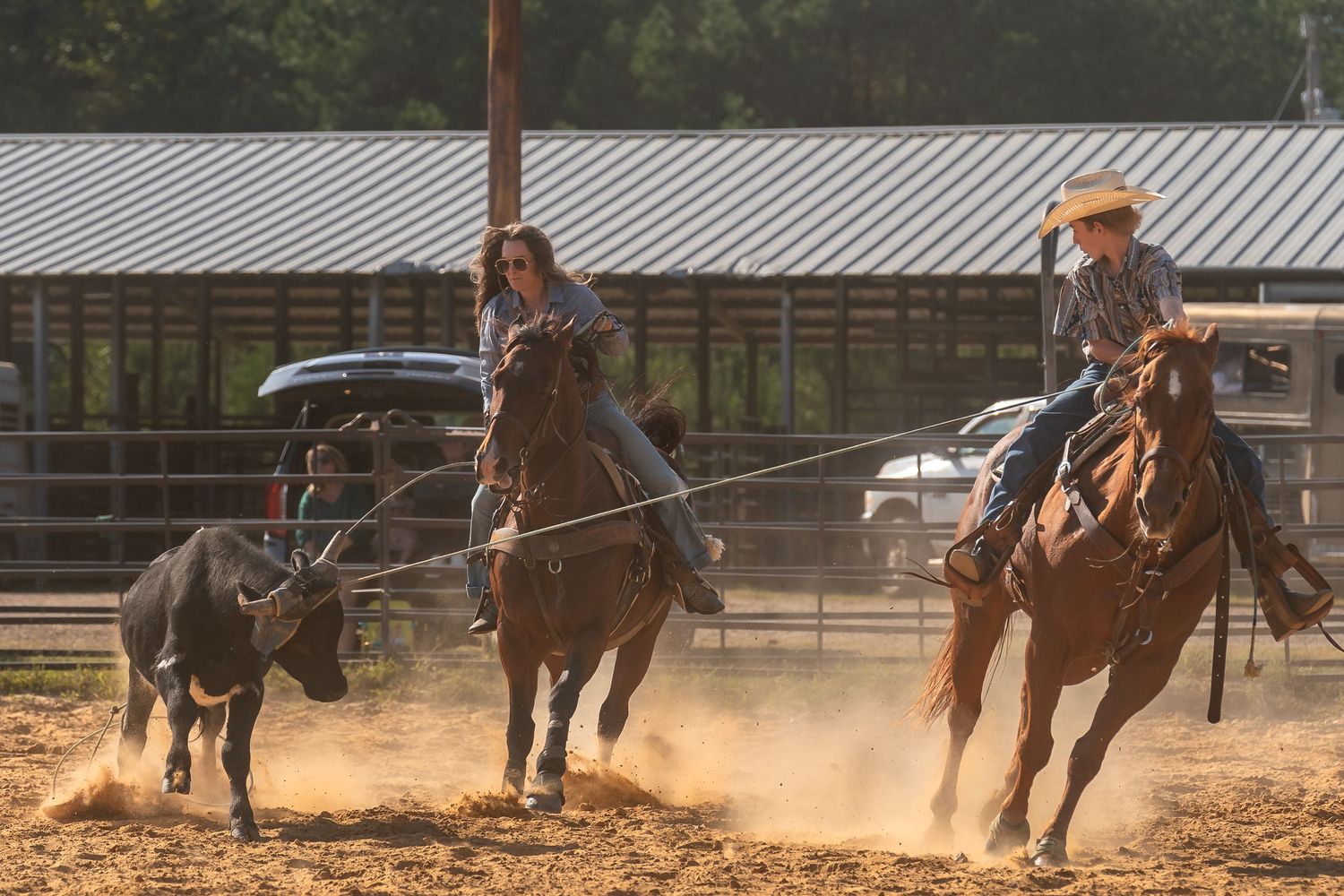 Team of riders chase calf with lassos in dusty outdoor arena.