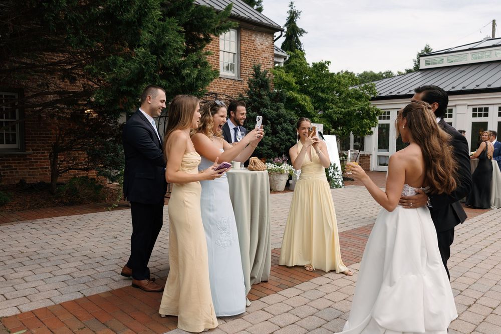 Bridesmaids in yellow dresses and guests gather outdoors at an elegant brick venue wedding cocktail hour.